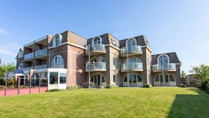 Een meerlaags woongebouw met balkons, een overdekt terras en een verzorgd gazon.