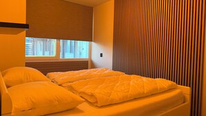 A bedroom with a bed, pillows, a window, and a wall with vertical lines. - Holiday home Residenz Polderblick 3 in Burgerbrug. Suitable for 4 people, 2 bedrooms. (Burgerbrug)