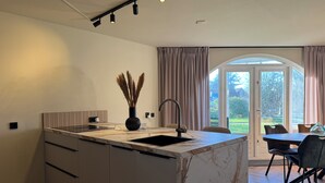 A modern kitchen with a marble island, a built-in sink, and a dining area with a table and chairs. - Holiday home Residenz Polderblick 3 in Burgerbrug. Suitable for 4 people, 2 bedrooms. (Burgerbrug)