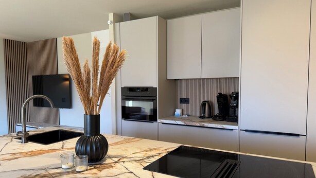 A modern kitchen with a marble countertop, a black sink, a built-in oven, a coffee maker, and a vase with dried plants. - Holiday home Residenz Polderblick 3 in Burgerbrug. Suitable for 4 people, 2 bedrooms. (Burgerbrug)