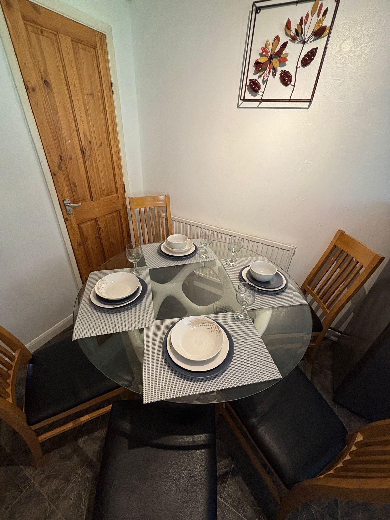 Ett matbord med plats för fyra personer, inklusive stolar, en trädörr och en inramad tavla på väggen.