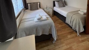 A small, cozy room with two single beds, a bedside table with a lamp, and a window with curtains. - use With Modern Comforts (Nottingham)