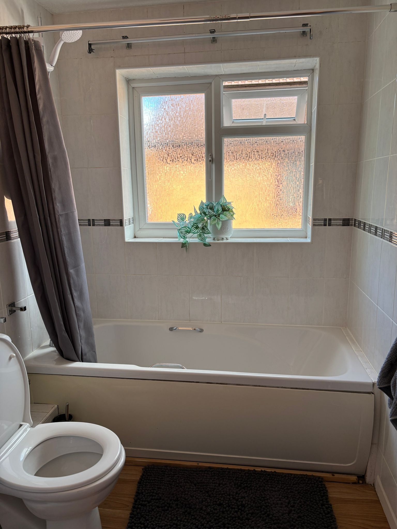 Un baño con bañera, inodoro, ventana con planta y cortina de ducha.