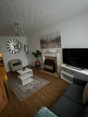 Ein Wohnzimmer mit Kamin, Fernseher, Sofa, Couchtisch und einem gemusterten Teppich.