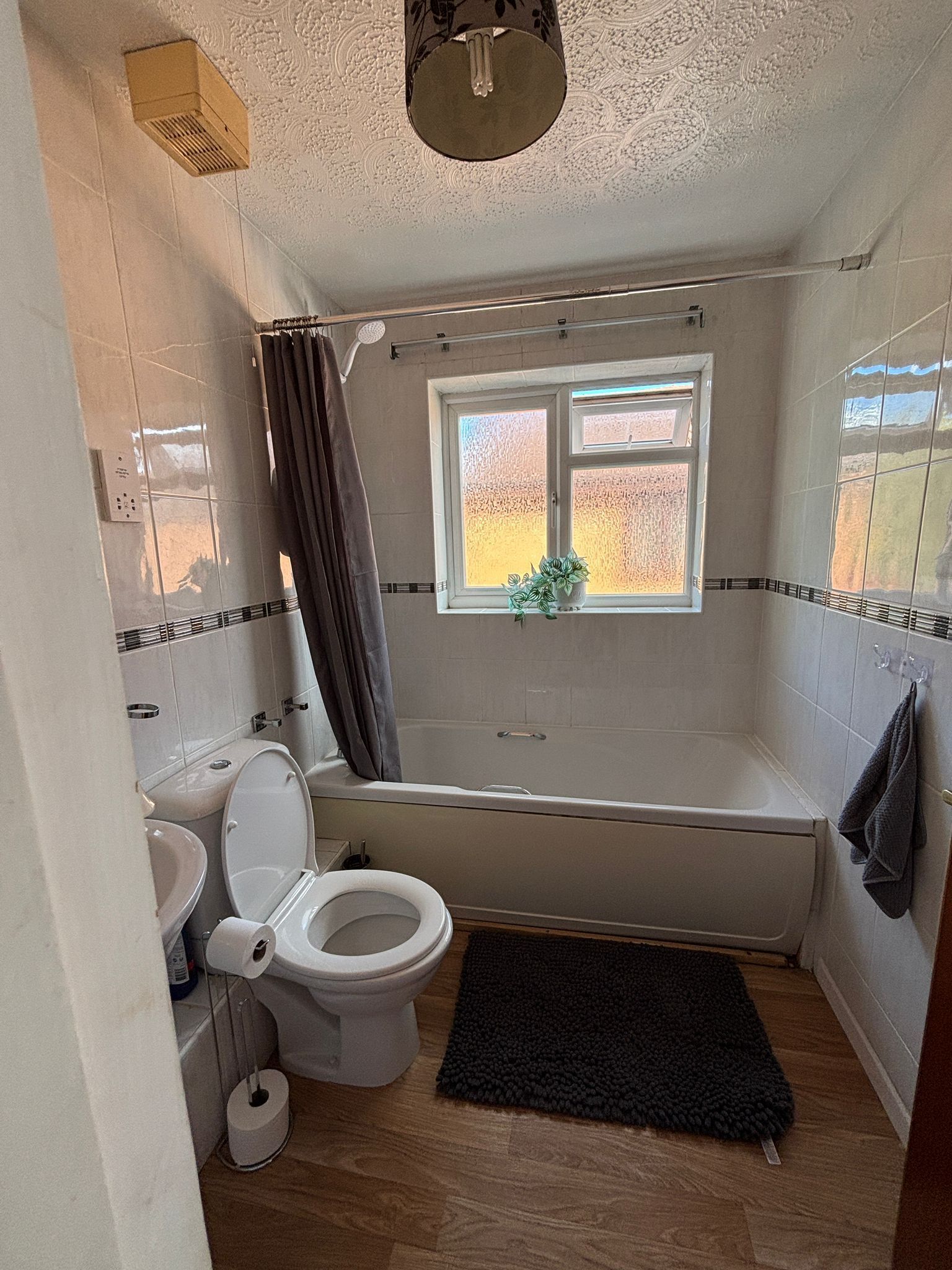 A bathroom with a toilet, bidet, bathtub, and a window with a view.