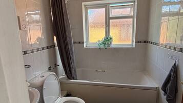 A bathroom with a toilet, bidet, bathtub, and a window with a view.