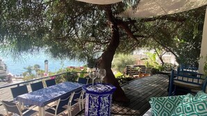 A wooden deck with a table and chairs, a small decorative table, and a bench with cushions. - CASA EVASION at the foot of the beach, incredible views surrounded by a beautiful garden. (Almuñécar)