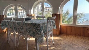 A dining area with a table covered in a floral tablecloth, surrounded by white chairs, large arched windows with a view of the sea, and wooden paneling on the walls. - CASA EVASION at the foot of the beach, incredible views surrounded by a beautiful garden. (Almuñécar)
