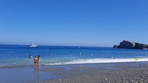 A beach with a rocky shoreline, clear blue water, and a few people in the distance. - CASA EVASION at the foot of the beach, incredible views surrounded by a beautiful garden. (Almuñécar)