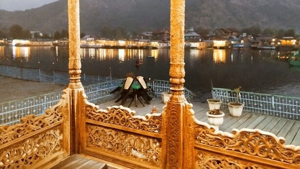 A wooden gazebo with intricate carvings overlooking a calm body of water with a mountain in the background. - DeLaila Luxury Houseboat by Shahnawaz  (Srinagar)