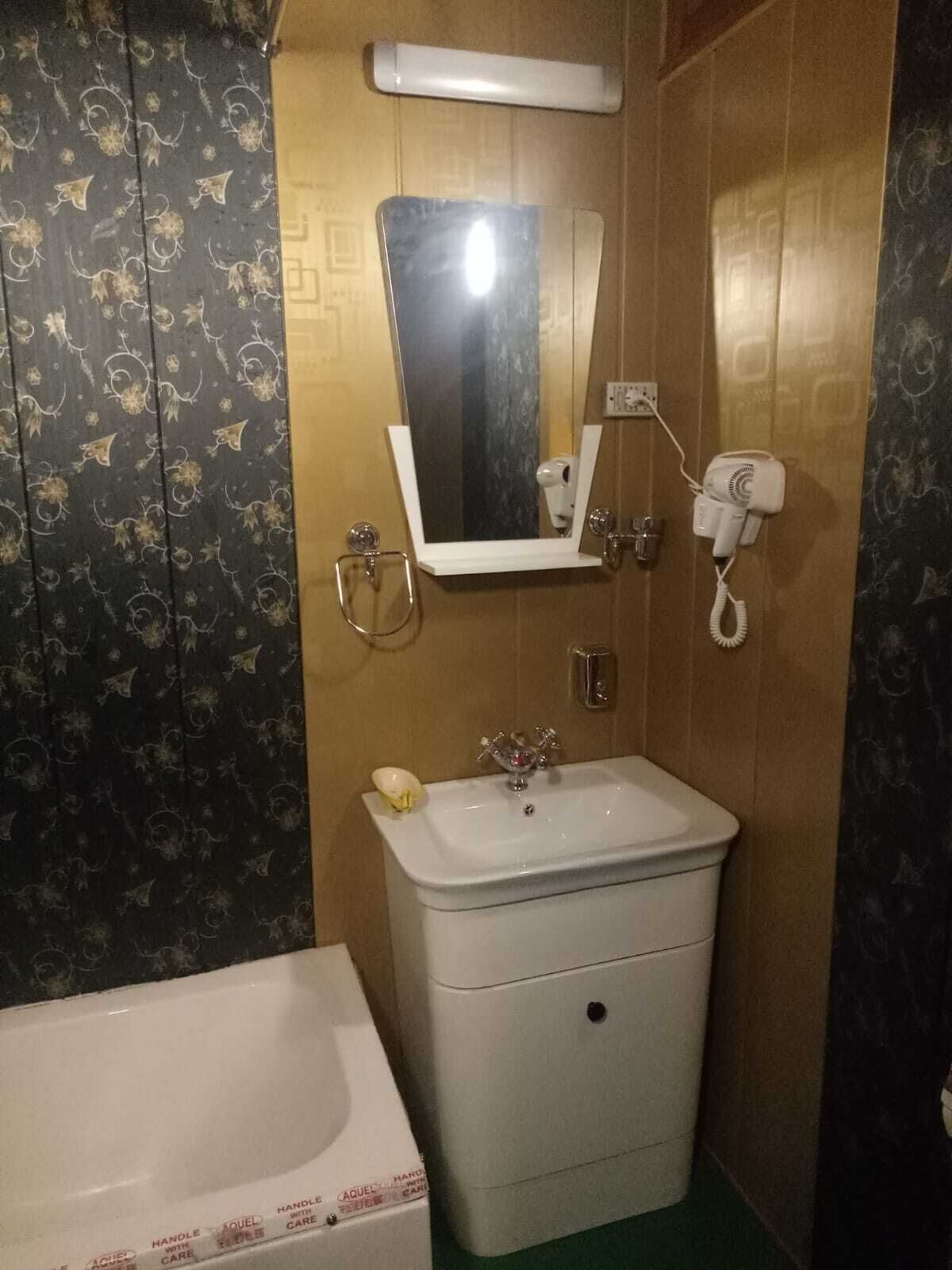 Uma casa de banho com uma pia branca, um espelho em cima, um secador de cabelo na parede e uma banheira.