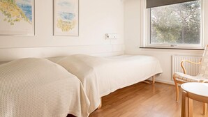 Une chambre avec deux lits simples, un plancher en bois, une fenêtre donnant sur la forêt et deux œuvres d’art encadrées accrochées au mur.