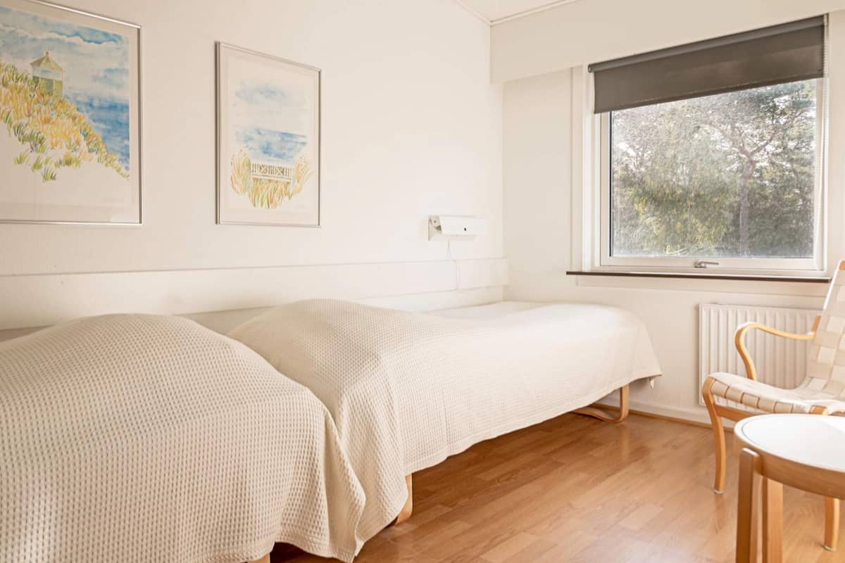 Ein Zimmer mit zwei Einzelbetten, Holzboden, Fenster mit Blick auf Bäume und zwei gerahmte Kunstwerke an der Wand.
