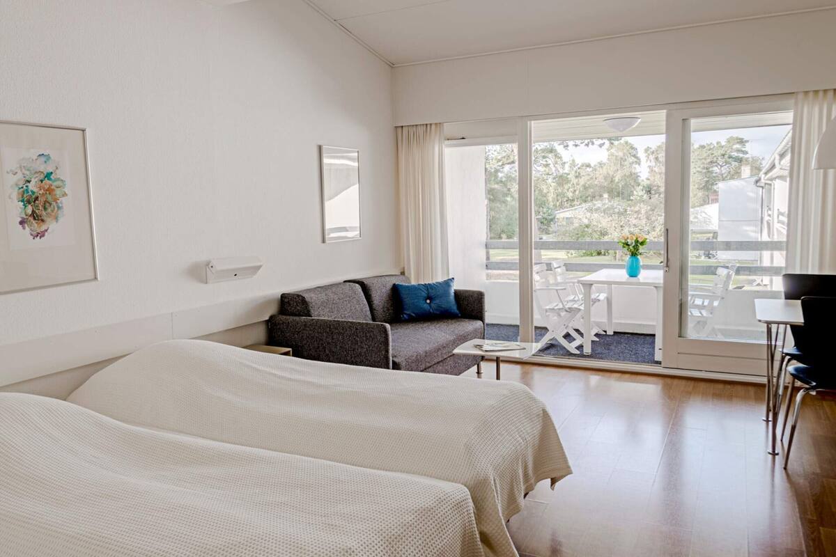 Ein Hotelzimmer mit zwei Betten, einem Schlafsofa, einem Tisch und einem Balkon mit Blick.