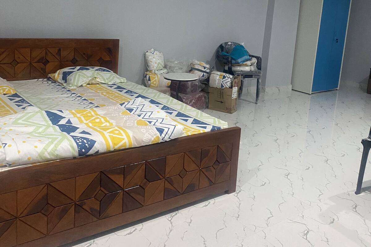A bedroom with a bed, a ceiling fan, an air conditioner, a wardrobe, and a small table with items on it.