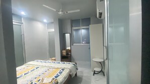 A bedroom with a bed, a ceiling fan, a window, and a small table. - Vishal Banquet & Marriage Hall (Bodh Gaya)