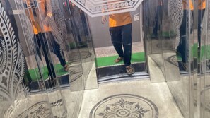 A person standing in a glass elevator with a patterned floor and a green mat at the base. - Vishal Banquet & Marriage Hall (Bodh Gaya)
