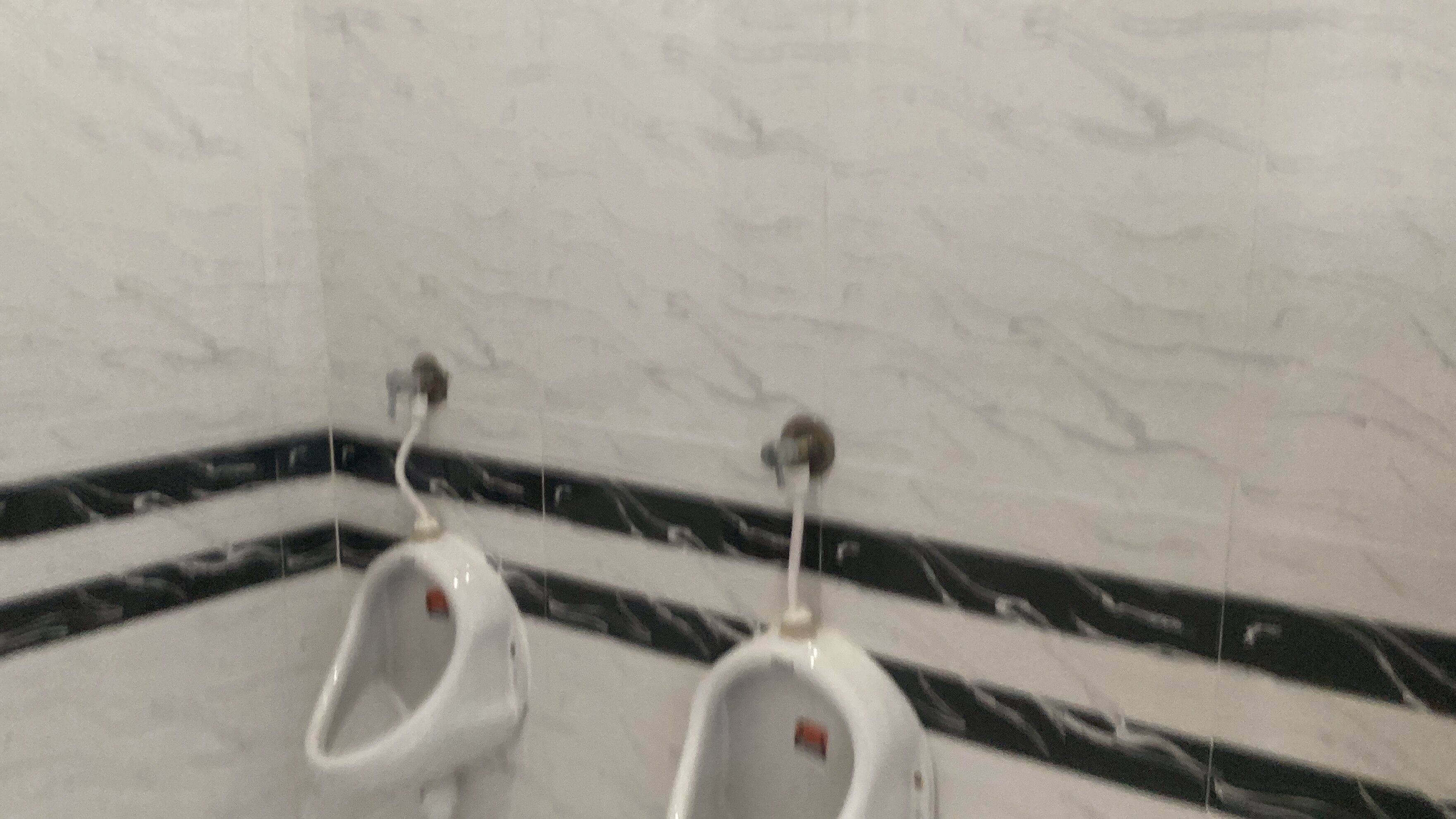 A restroom with two urinals, a marble wall, and a black and white patterned floor.
