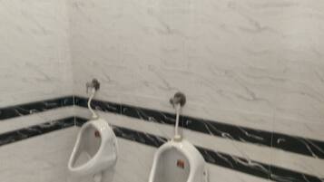 A restroom with two urinals, a marble wall, and a black and white patterned floor.