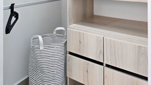 En garderob med flera hyllor och plats för att hänga kläder, en randig väska och ett metallställ.