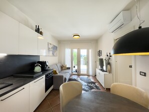 Una cucina compatta con elettrodomestici moderni, un'area pranzo con tavolo e sedie e vista all'esterno tramite una porta vetrata.