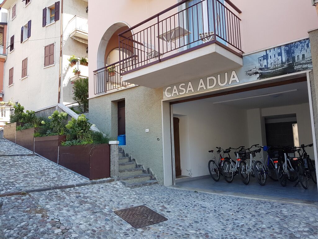 A building named "CASA ADUA" with a covered entrance, a staircase, and several bicycles parked outside.