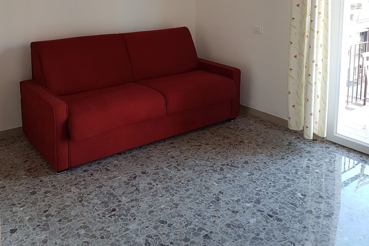 A room with a red sofa, a wall clock, and a patterned curtain.