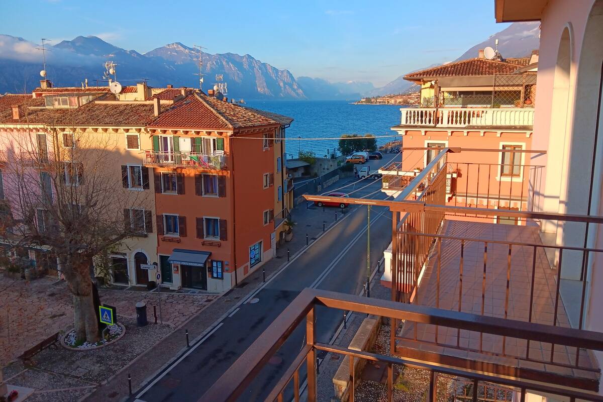 A coastal street with buildings, a clear sky, and mountains in the background.