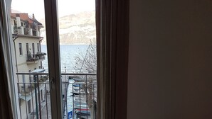 Een kamer met een grote schuifglazen deur die leidt naar een balkon met uitzicht op een waterpartij en een gebouw met balkons.