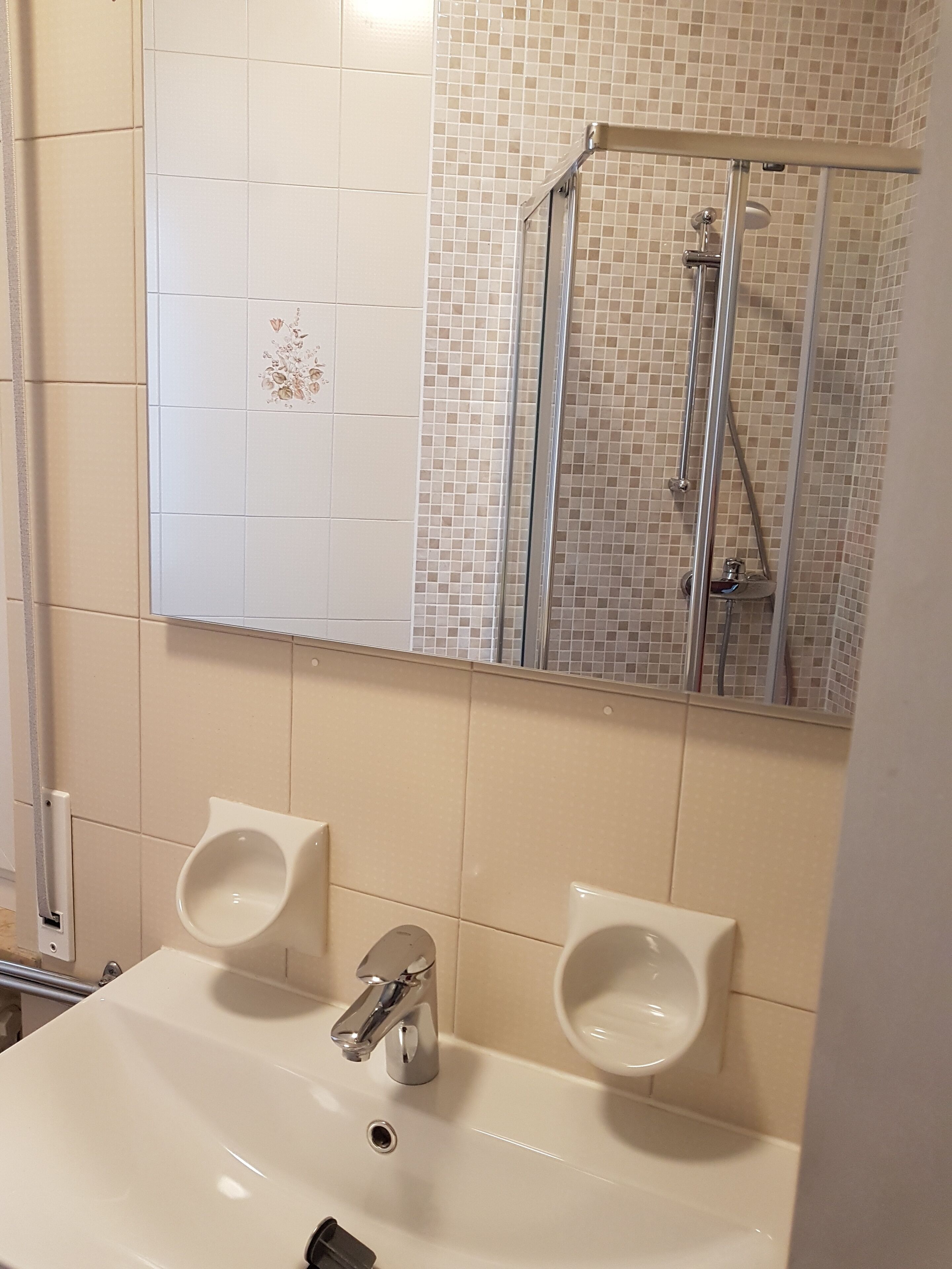Et badeværelse med håndvask, to pissoirer, bruser og spejl.