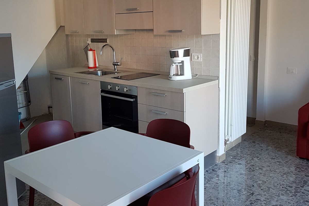 A compact kitchen with a dining area, including a table and chairs, a coffee maker, and a red chair.