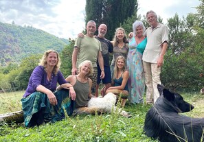 Eine Gruppe von Personen in einer Freiluftumgebung mit Rasenfläche, Bäumen und einer Hügelkulisse im Hintergrund.