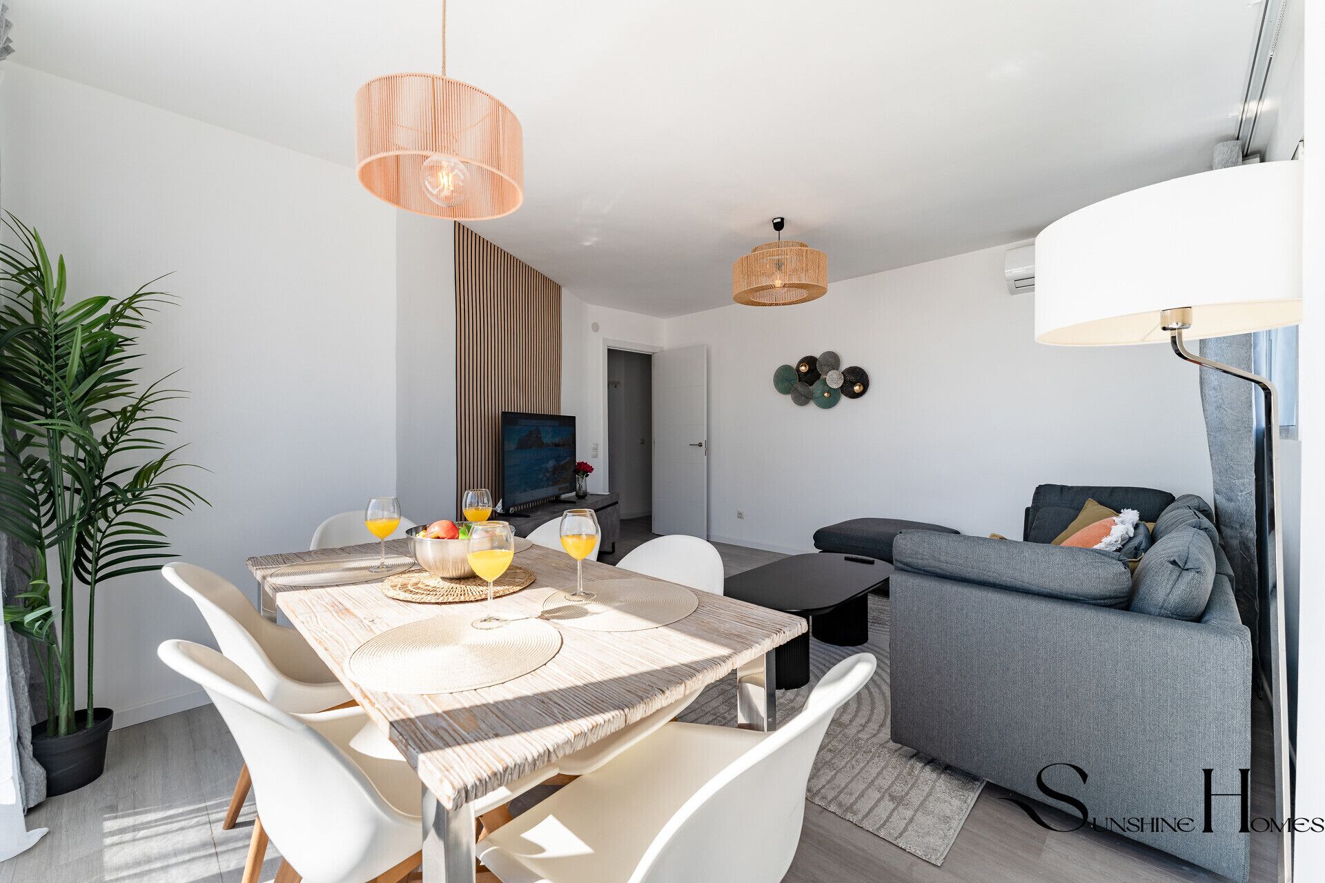 Una sala de estar moderna con comedor, que incluye una mesa de madera, sillas blancas, un sofá gris y un ventanal grande.