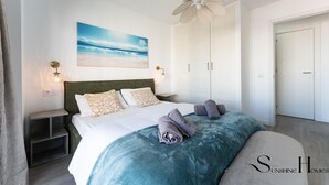 Ein Schlafzimmer mit einem Bett, einem Deckenventilator, einem Strandbild und einem Kleiderschrank.
