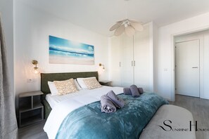 A bedroom with a bed, a ceiling fan, a painting of a beach, and a wardrobe. - Exclusive 3BR Near Beach & Puerto Marina REF069 (Benalmádena)