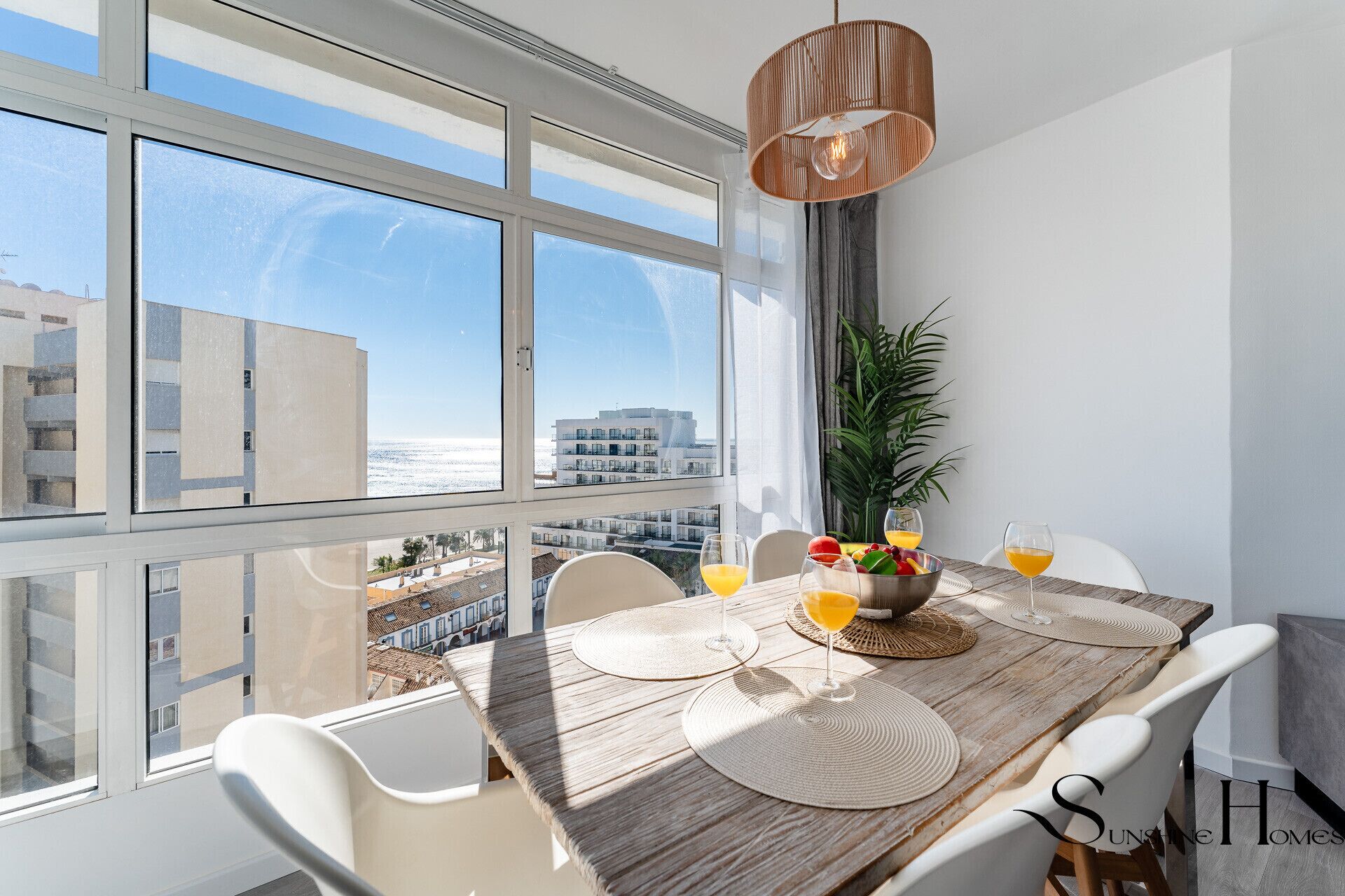 A dining area with a wooden table, white chairs, and a view of the city through large windows.