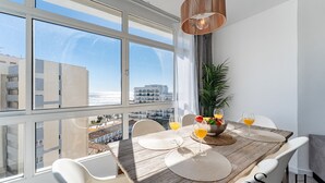 Ein Essbereich mit Holztisch, weißen Stühlen und Blick auf die Stadt durch große Fenster.