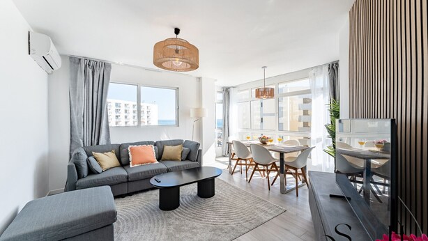 Ein modernes Wohnzimmer mit einem grauen Sofa, einem Couchtisch und einem Essbereich mit Tisch und Stühlen.
