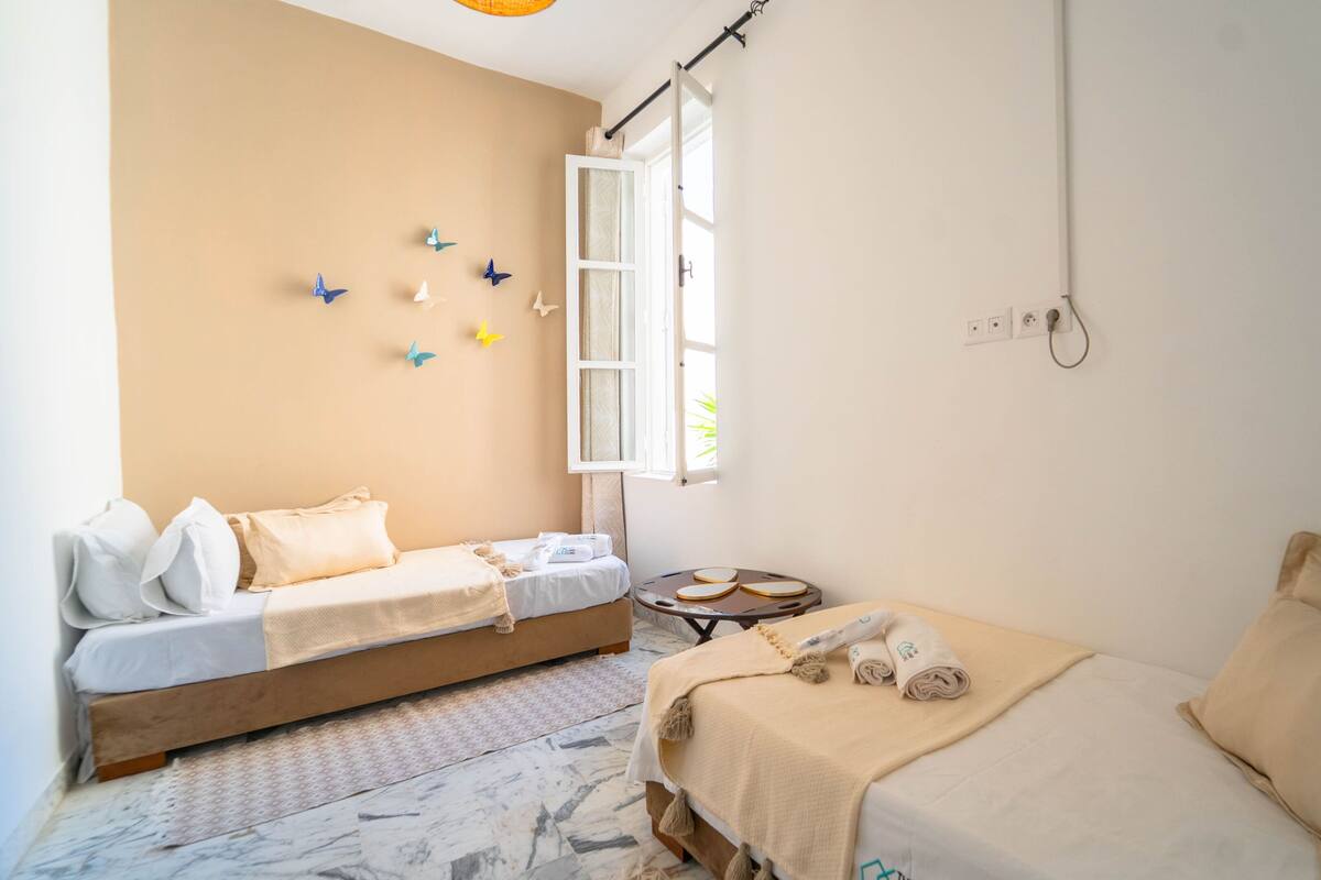 Una stanza piccola e luminosa con due letti, un tavolino e una finestra.