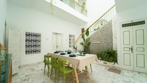 A dining area with a table set for four, surrounded by green chairs, a staircase, and a white wall with decorative patterns. - Dar Majoul (Tunis)