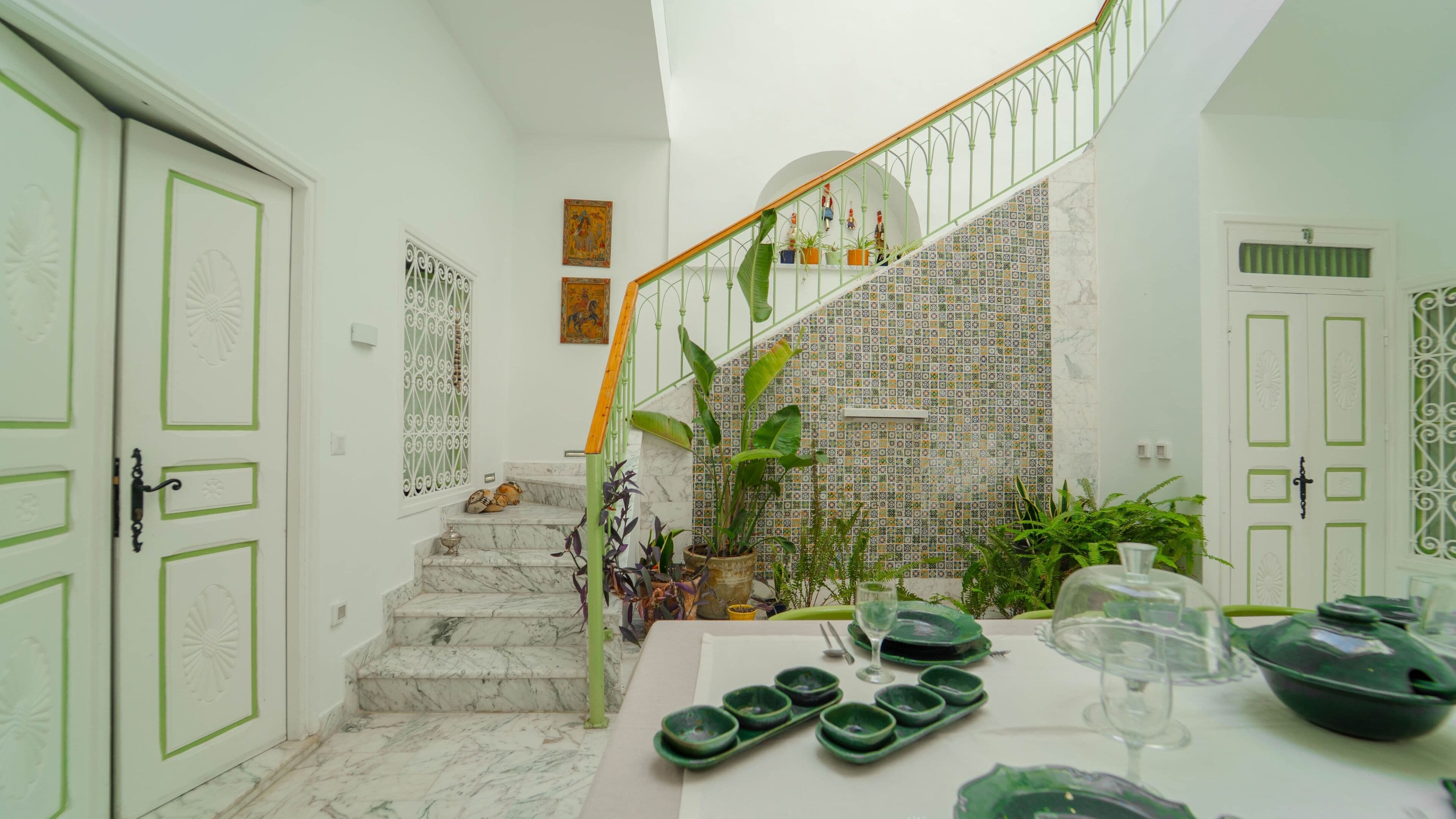 Un escalier avec une rampe verte menant à un palier doté d’un mur carrelé et de plantes en pot.