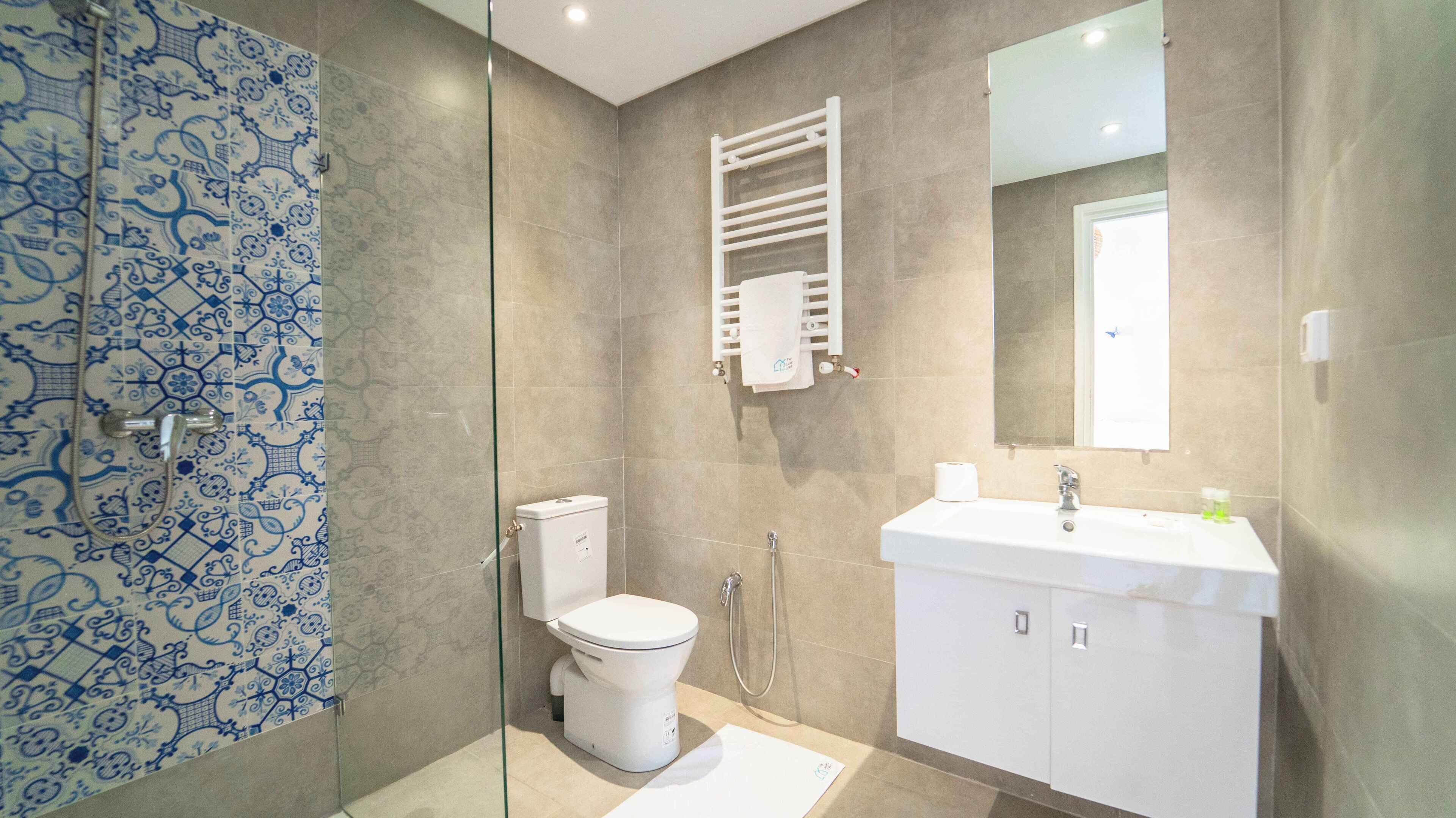 A bathroom with a glass shower enclosure, a toilet, a sink with a mirror, and a towel rack.