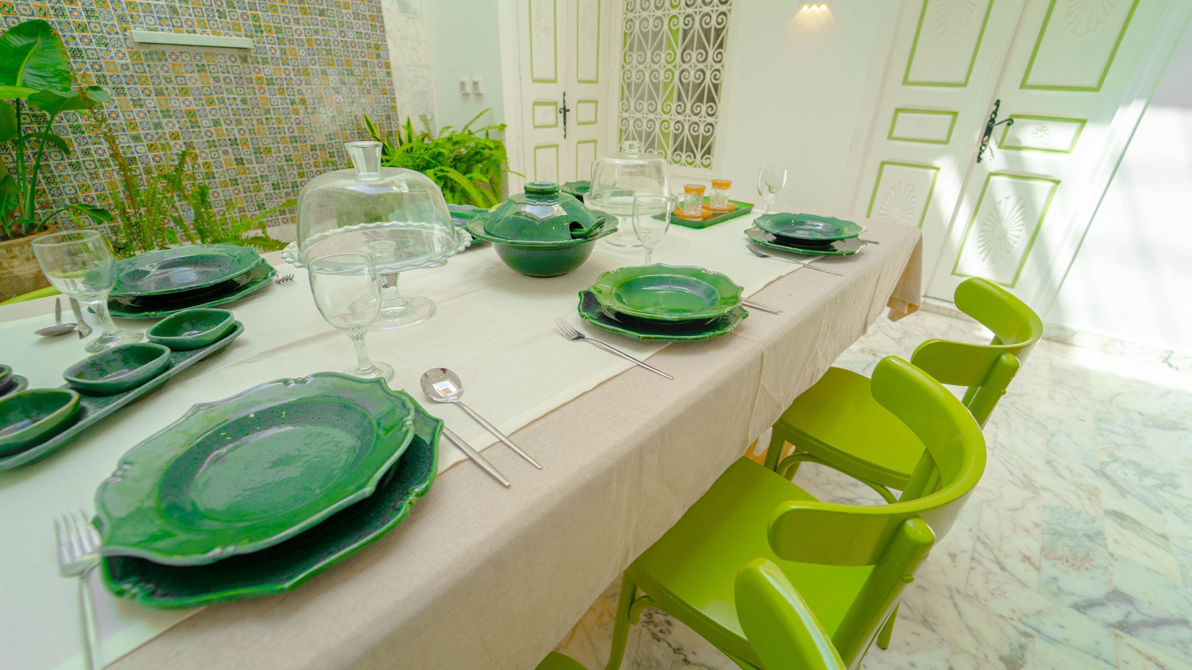 Mesa de comedor servida con platos, vasos y cubiertos verdes, rodeada de sillas verdes.