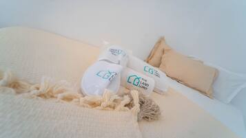 Ein Bett mit einer beigen Decke, zwei weiße Slipper mit blauer Aufschrift und ein beiges Kopfkissen.