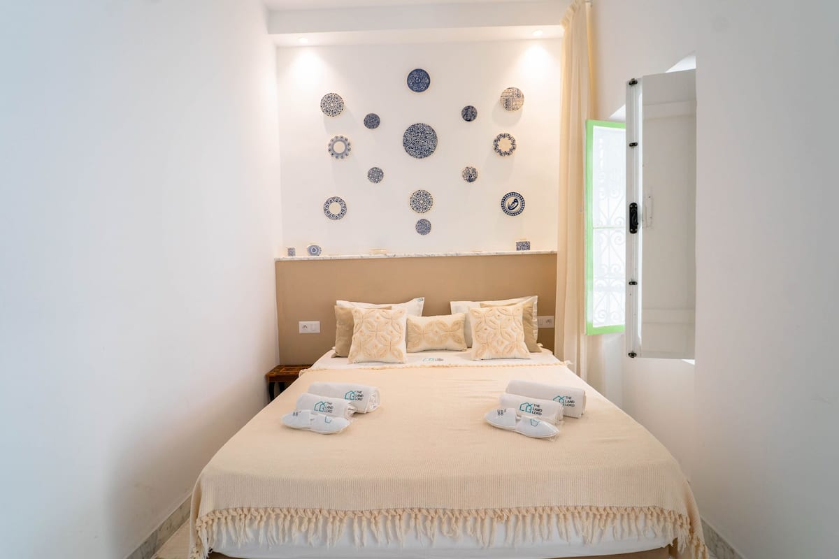 Una camera da letto ordinata con un letto, cuscini e un comodino.