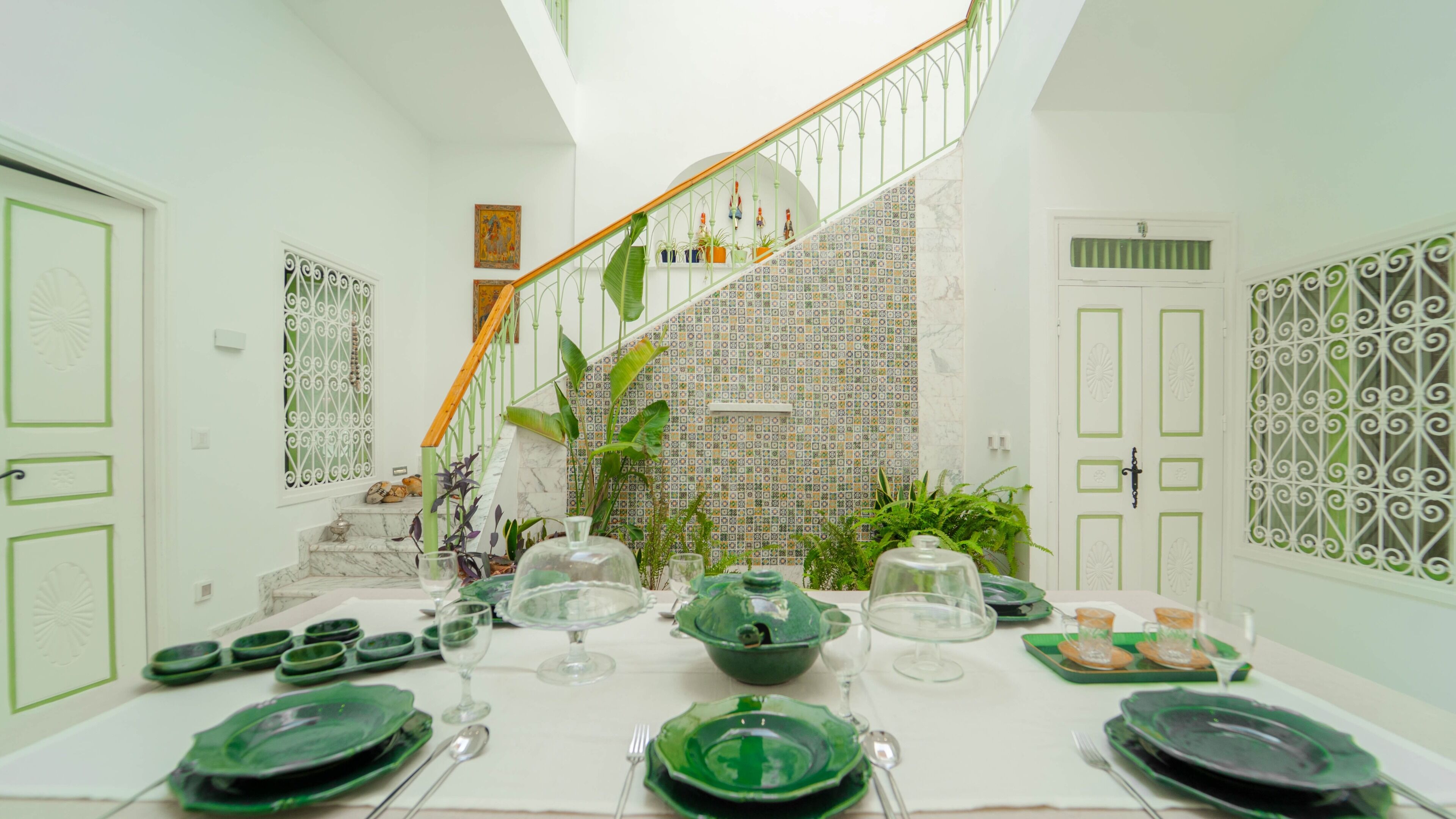 Un coin repas avec une table mise pour le repas, un escalier agrémenté de rampes décoratives et des murs à motifs.