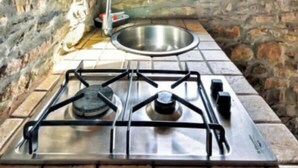 Una cucina con pareti in pietra, dotato di piano cottura a gas, lavello e finestra con vista sul paesaggio.