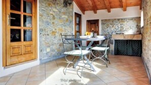 Una cucina rustica con pareti in pietra, travi in legno e un'area pranzo con sedie in metallo.