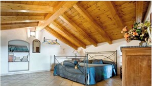 Una camera da letto con soffitto in legno, struttura del letto in metallo, comodino e mensola a parete con libri.