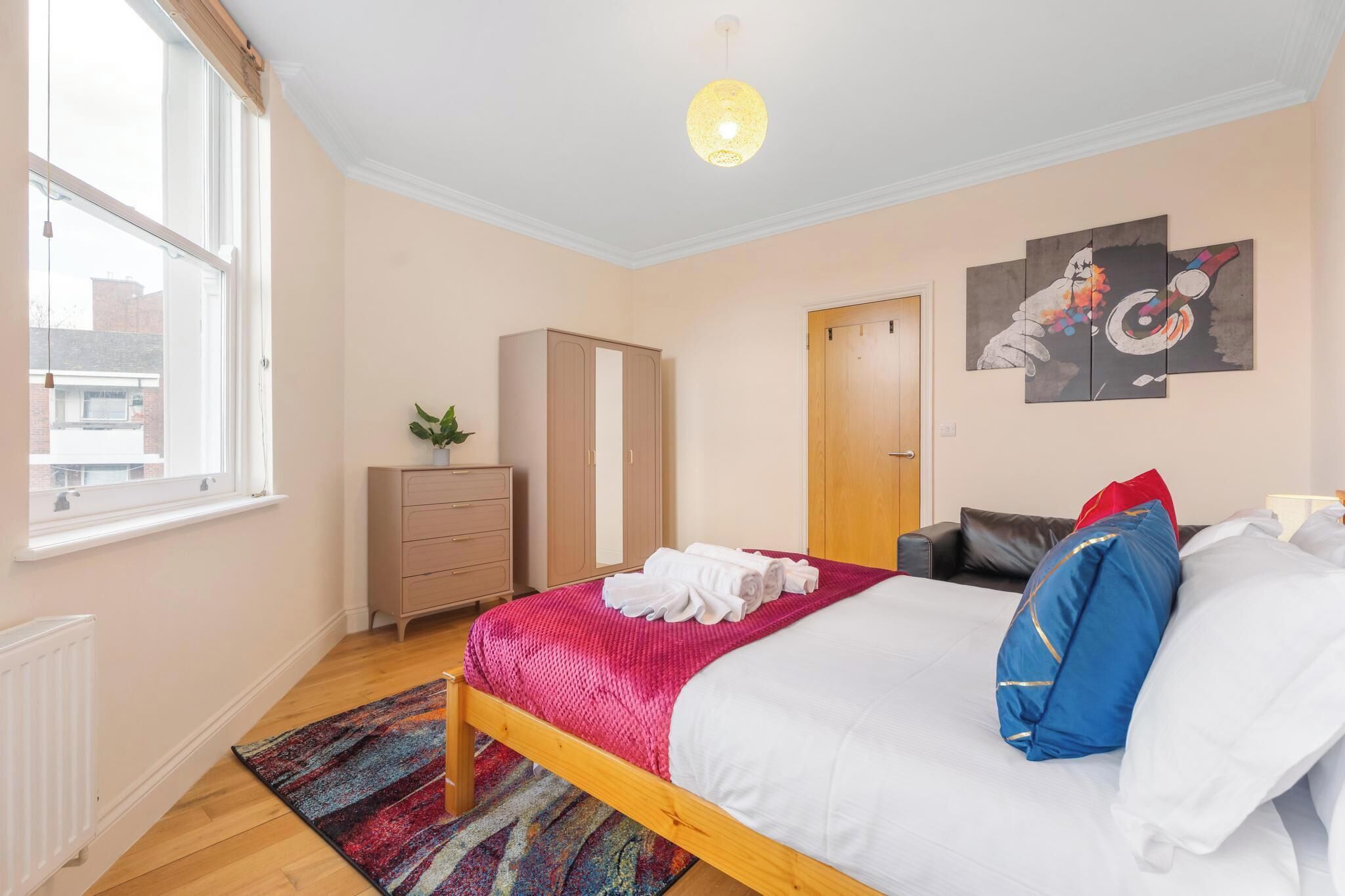 A bedroom with a bed, a wardrobe, a radiator, a window, and a door.